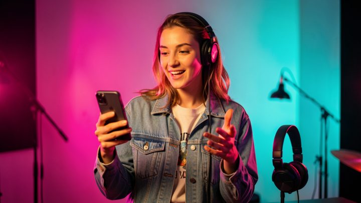Jeune musicienne présentant une nouvelle chanson avec un smartphone dans une ambiance colorée et créative.
